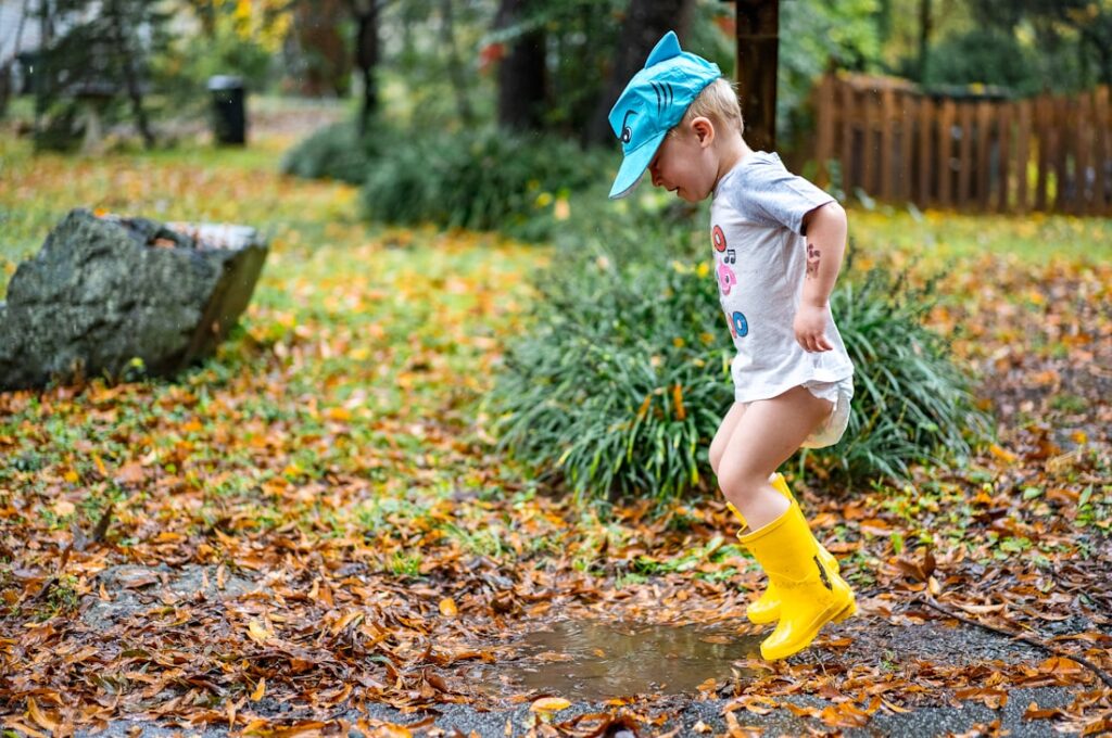 Enfant en bottes de pluie jaunes sautant dans une flaque parmi les feuilles d'automne